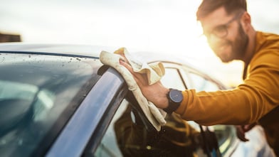 Shot of a happy young man cleaning his car with microfiber cloth on a sunny day.