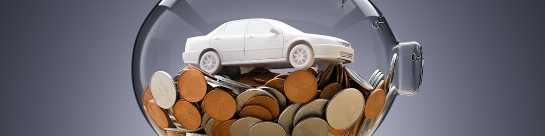 A white toy car sits inside a glass piggy bank filled with coins.