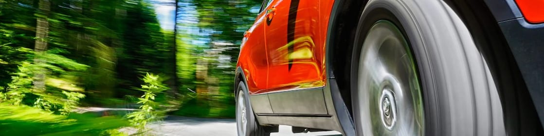A close-up angle of the front tyre on a red car driving through green scenery
