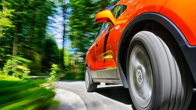 A close-up angle of the front tyre on a red car driving through green scenery