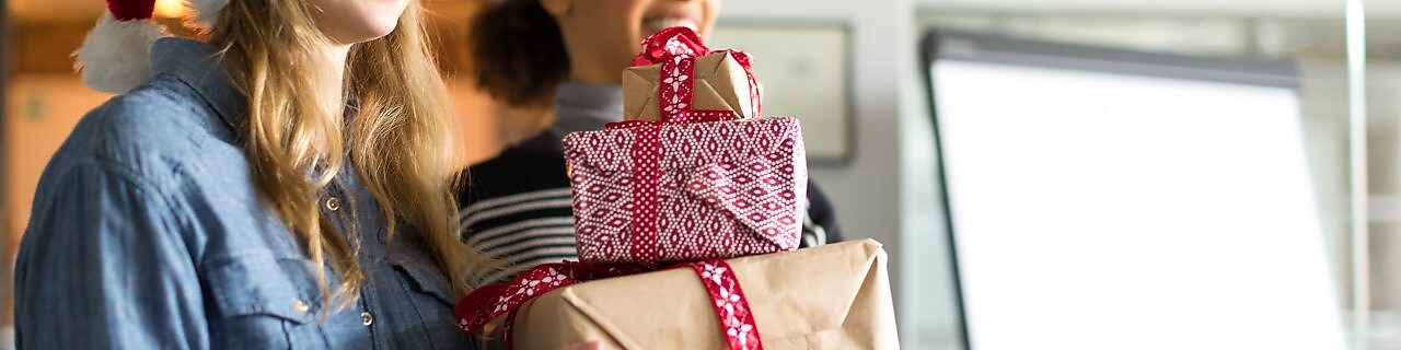 Two young females wearing Santa hats smile while holding three wrapped Christmas gifts.