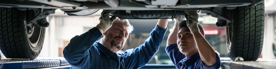 Two mechanics inspect the underside of a car.