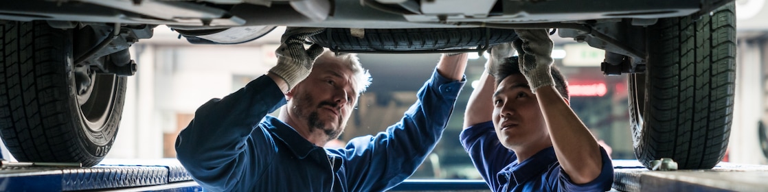 Two mechanics inspect the underside of a car.