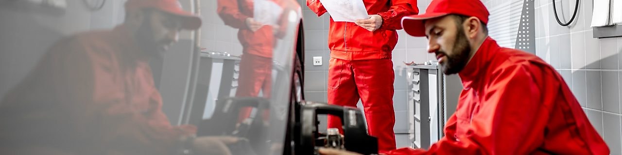 Two mechanics wearing red perform a wheel alignment.