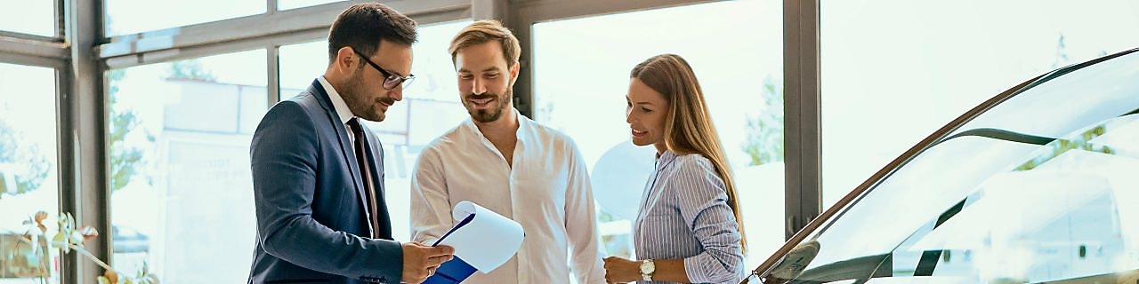 A man and woman review paperwork with a salesperson at a car dealership