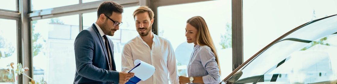 A man and woman review paperwork with a salesperson at a car dealership