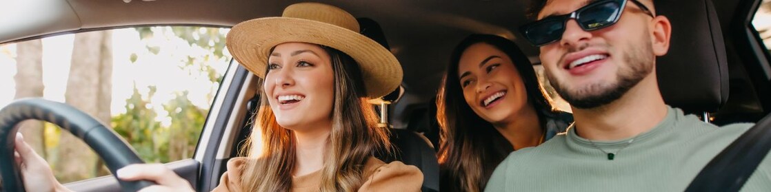 A group of three happy friends in a car on a road trip.