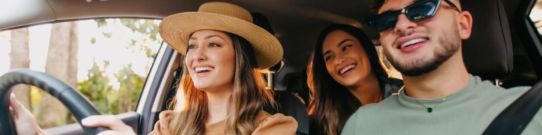 A group of three happy friends in a car on a road trip.