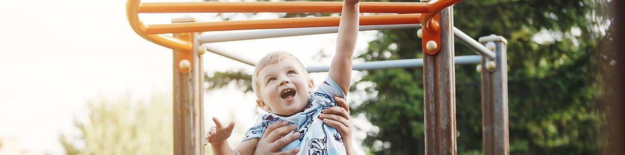 dad lifting and holding son on the monkey bars