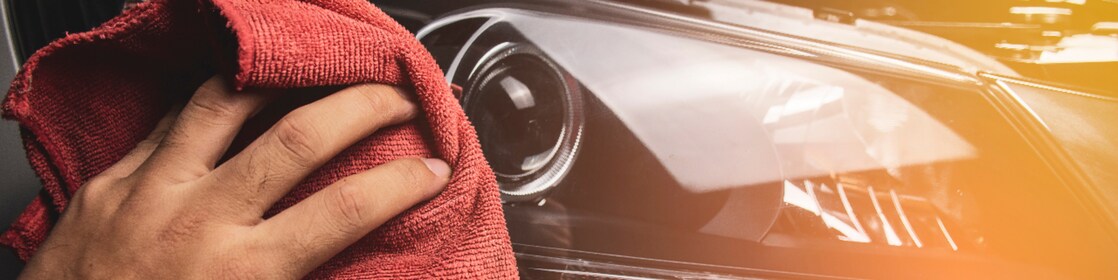 Hand cleaning a car headlight with a red microfiber cloth.