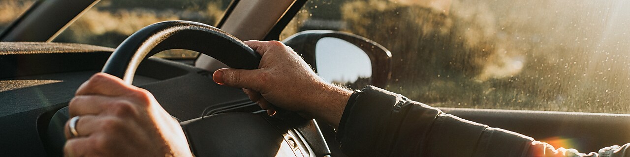 Hand holds a black steering wheel. Car is illuminated by low, warm sun at dusk.