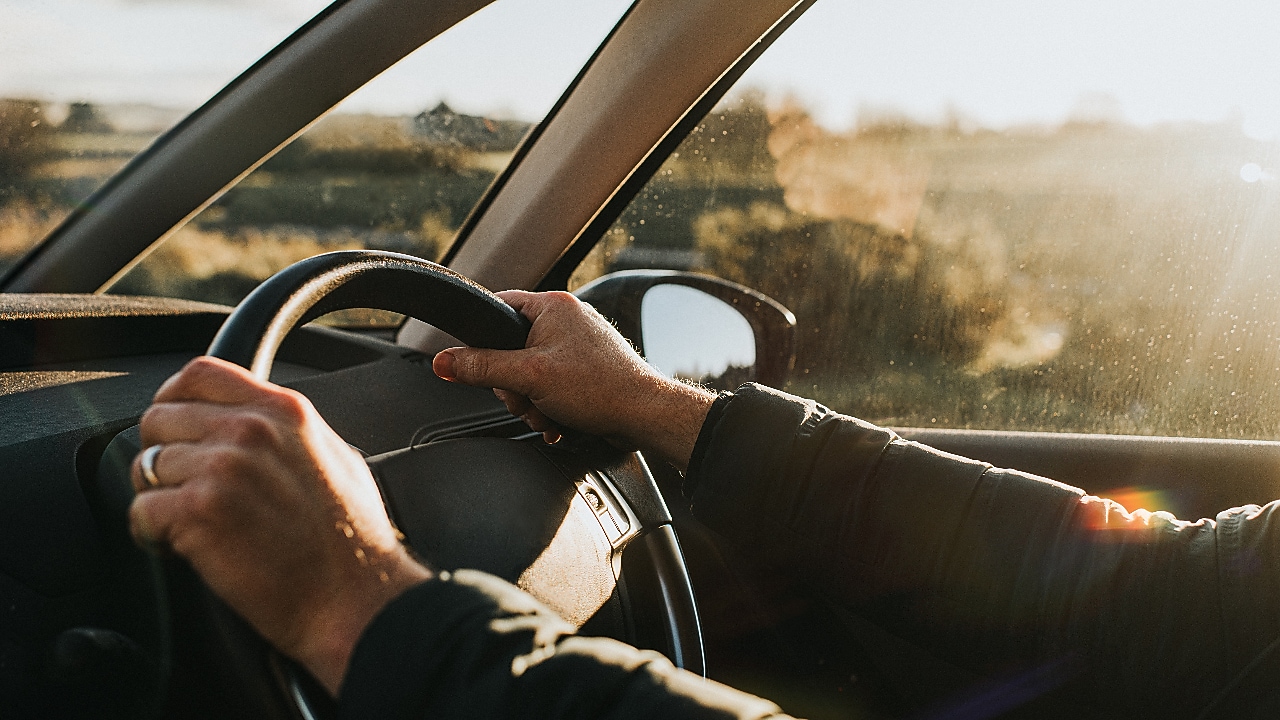 Hand holds a black steering wheel. Car is illuminated by low, warm sun at dusk.