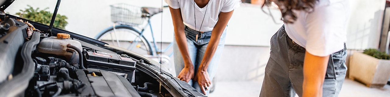 Hispanic mother watching her son check the oil in the car