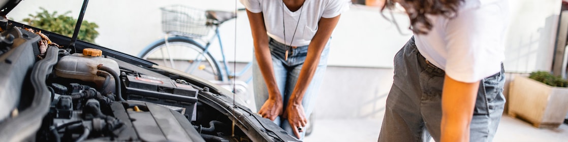 Hispanic mother watching her son check the oil in the car