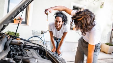 Hispanic mother watching her son check the oil in the car