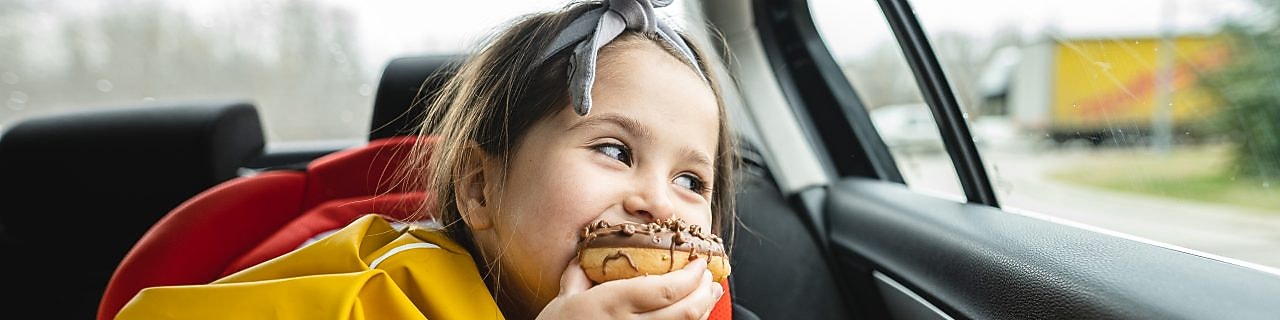 A child eating a donut and smiling inside a car