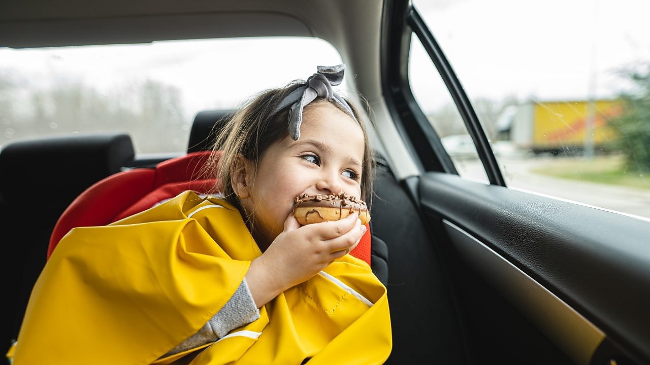 A child eating a donut and smiling inside a car
