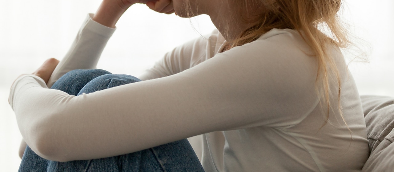 Young lady sitting on couch with knees tucked and face turned away
