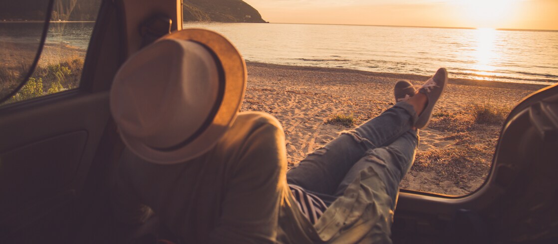 person sitting in the boot of the car looking out to a sunset on the beach