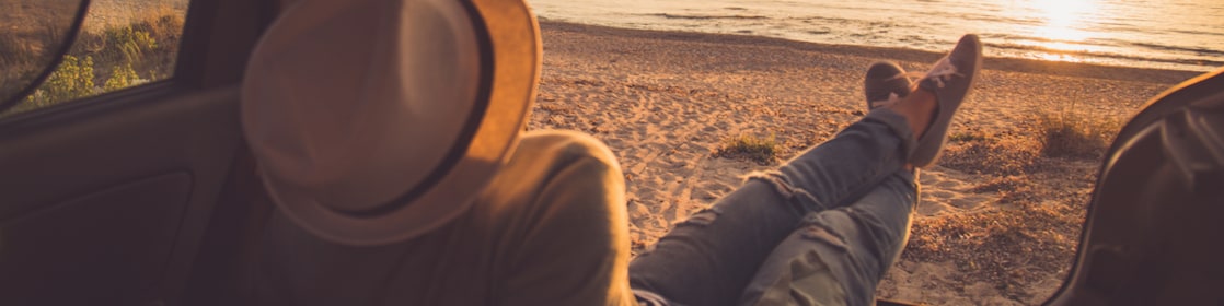 person sitting in the boot of the car looking out to a sunset on the beach