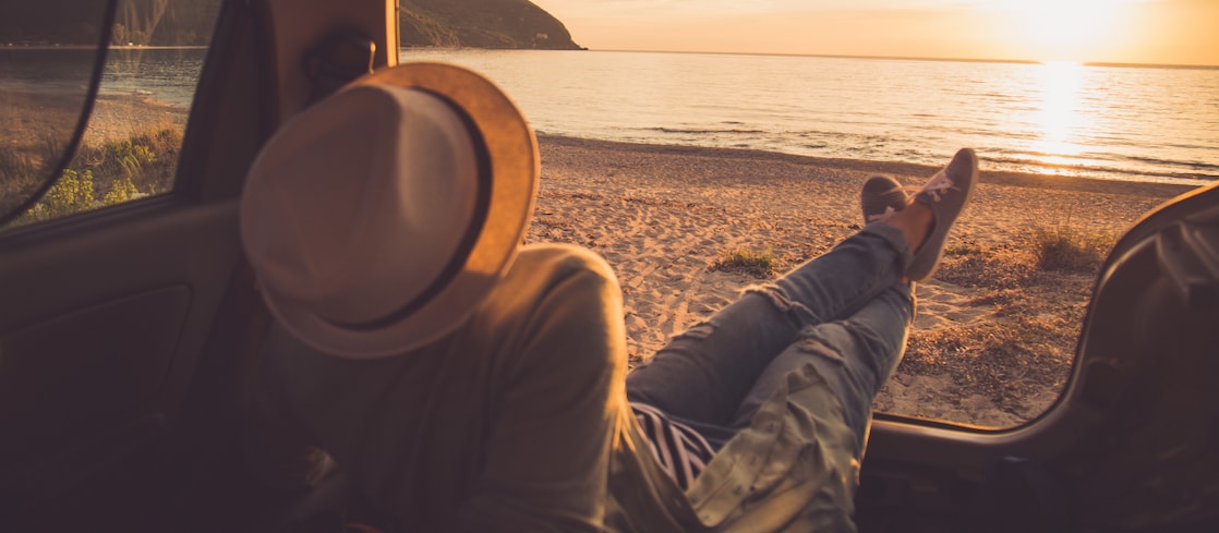 person sitting in the boot of the car looking out to a sunset on the beach