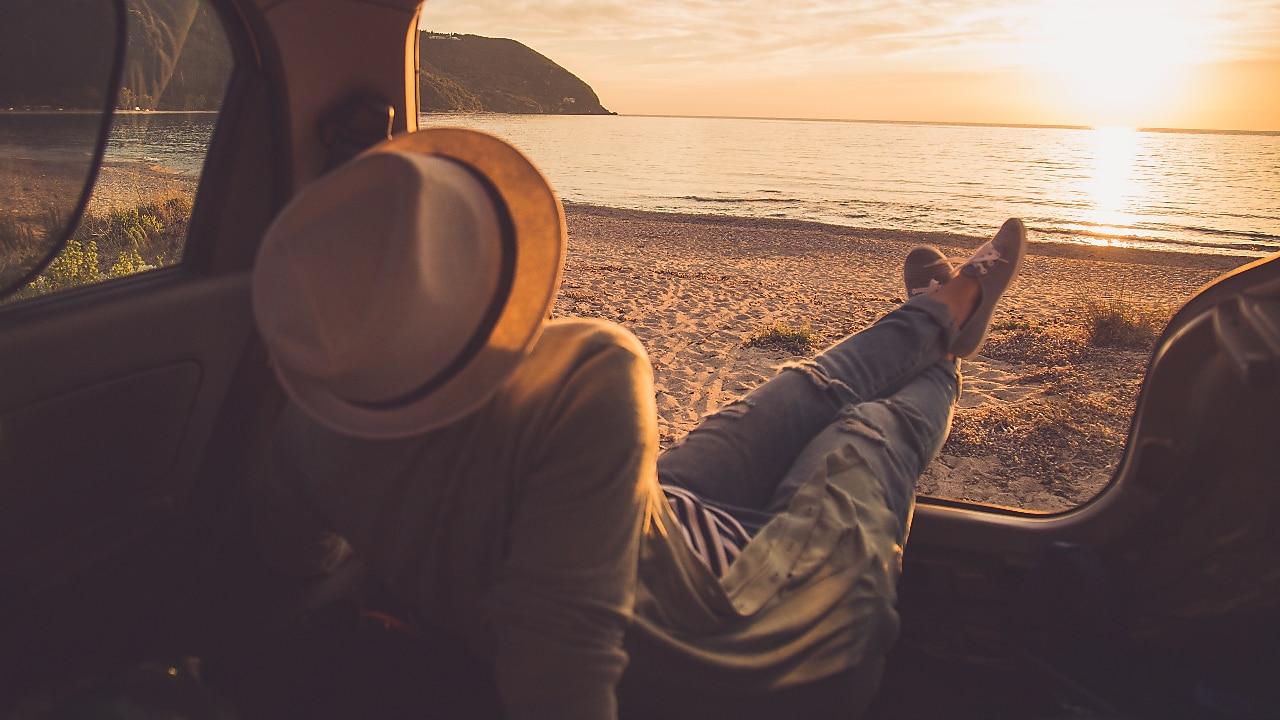 person sitting in the boot of the car looking out to a sunset on the beach