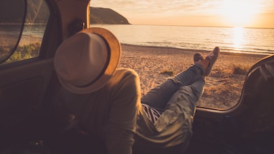 person sitting in the boot of the car looking out to a sunset on the beach