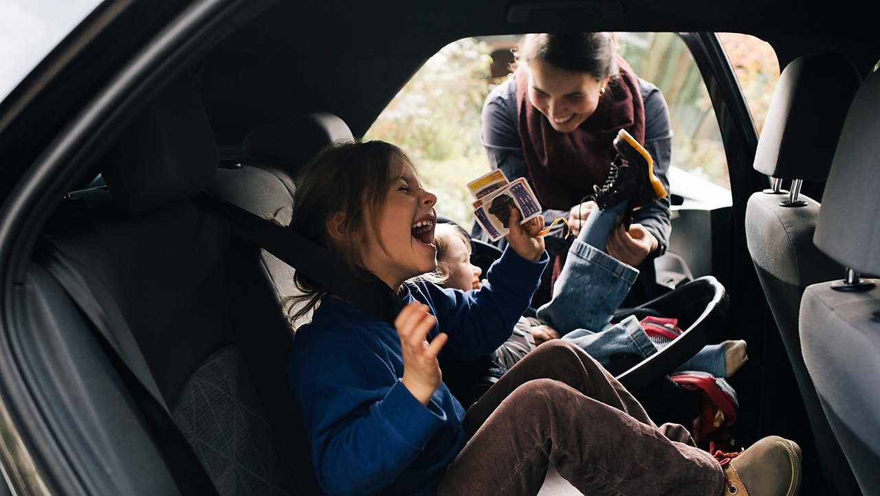 little girl laughing in the back of the car with mother in the background