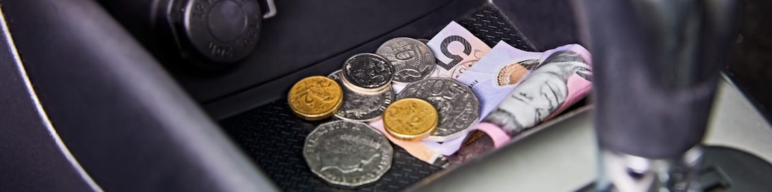 Multiple Australian coins and a five-dollar note lie in the front middle console of a car.