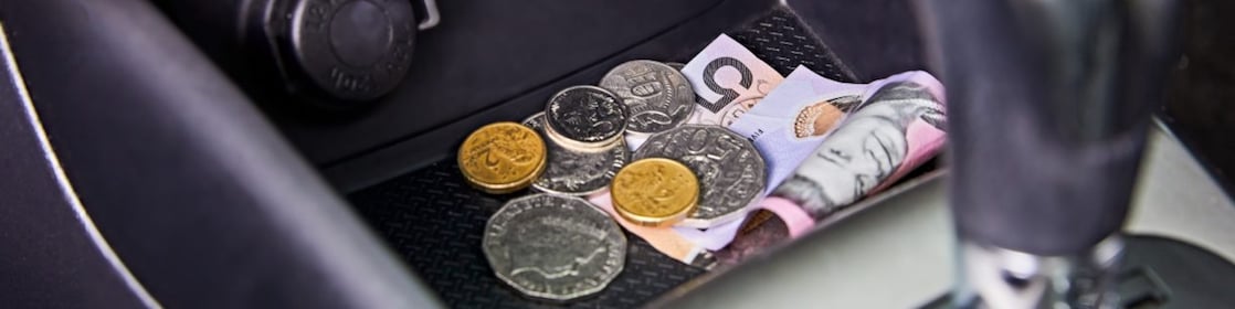 Multiple Australian coins and a five-dollar note lie in the front middle console of a car.