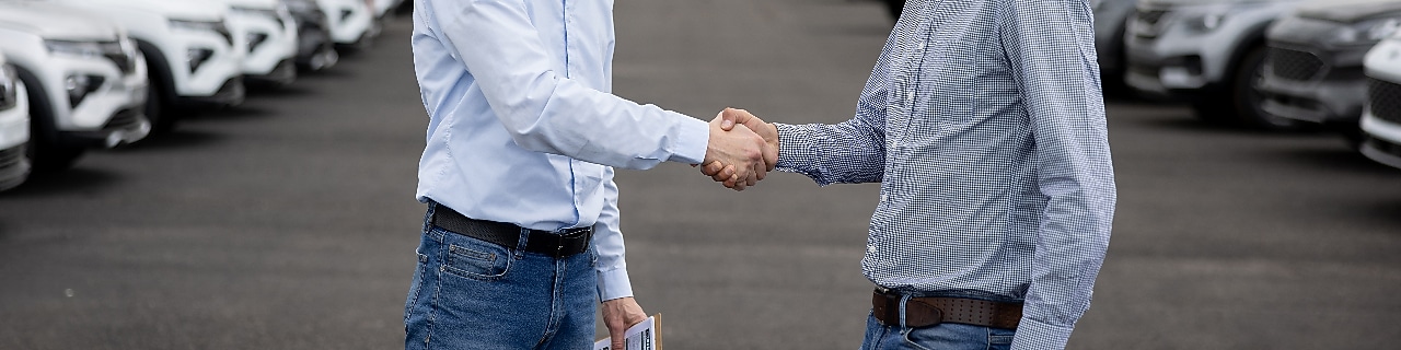 Two men shaking hands in a lot of parked cars