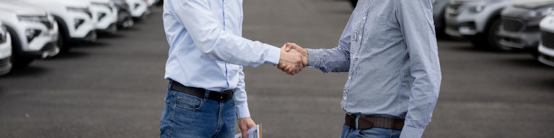 Two men shaking hands in a lot of parked cars