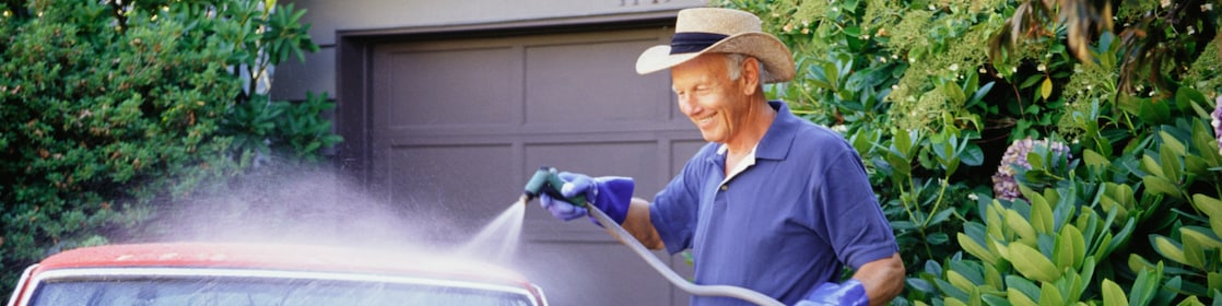 A man washes his vintage car in front of his garage.