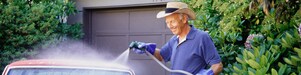 A man washes his vintage car in front of his garage.