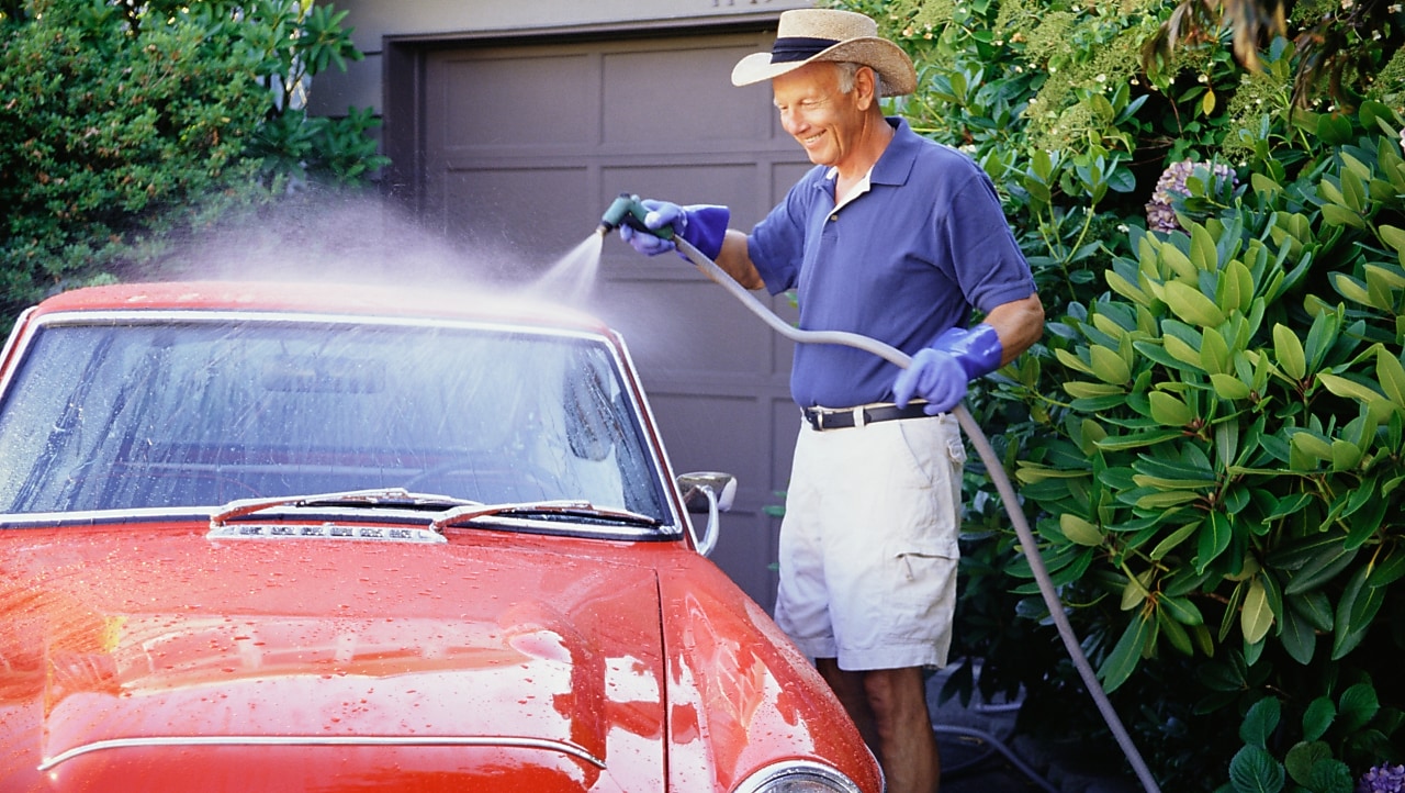 A man washes his vintage car in front of his garage.