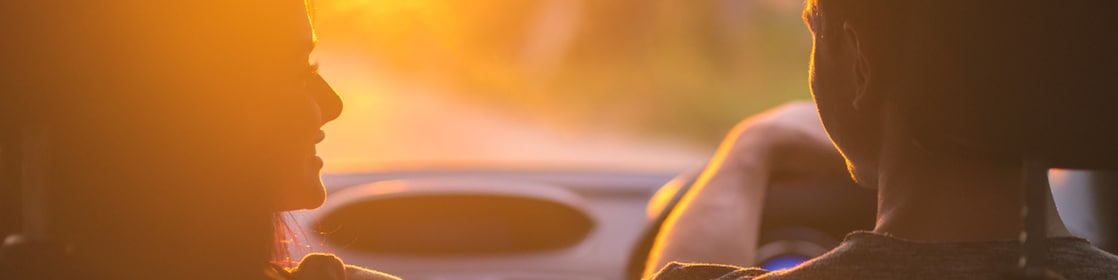 The couple drive a car on the background of the sunset