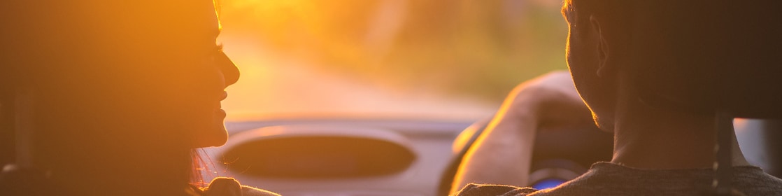 The couple drive a car on the background of the sunset