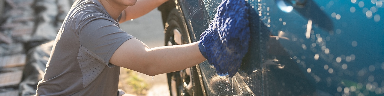 Young asian adult man washing car in yard
