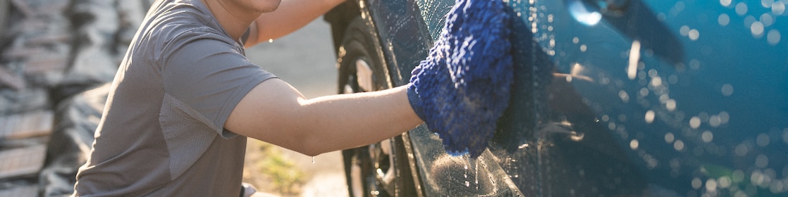 Young asian adult man washing car in yard