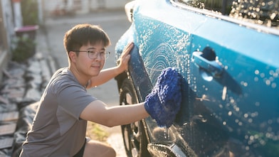 Young asian adult man washing car in yard