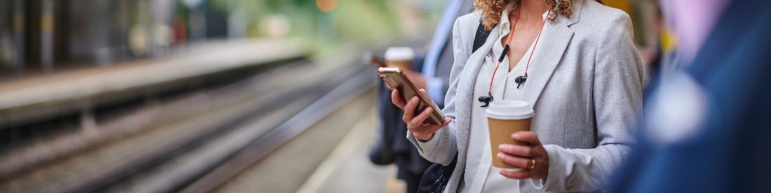 Woman waiting safety for train on her phone and coffee cup in hand
