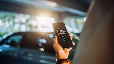 Over the shoulder view of young woman using mobile app device on smartphone to order a taxi pick up service in the city