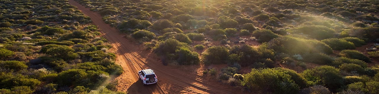 A truck navigates a rugged dirt road, surrounded by the vast expanse of a sunlit desert landscape.