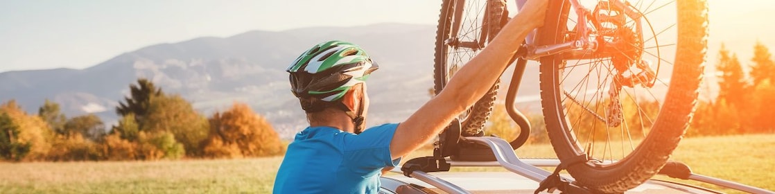 A cyclist taking his mountain bike from his car roof racks while looking into the distance.