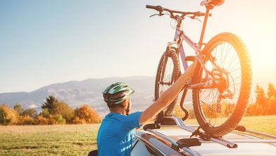 A cyclist taking his mountain bike from his car roof racks while looking into the distance.