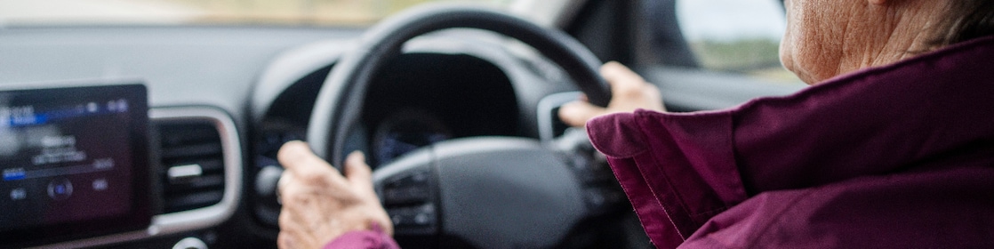 Over the shoulder view of a senior woman driving her car on a country road during a weekend getaway