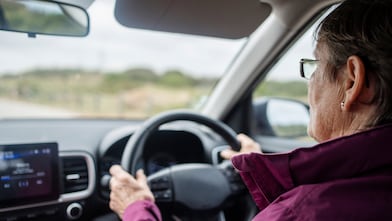Over the shoulder view of a senior woman driving her car on a country road during a weekend getaway