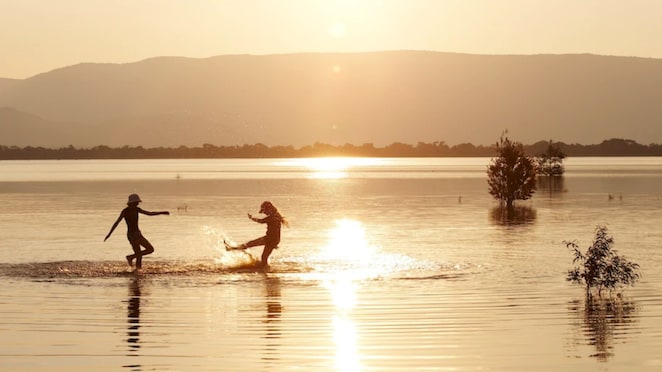 Two people playing in a lake during sunset
