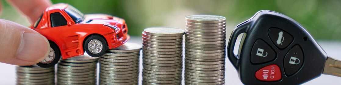 A hand places a toy car is over a stack of coins with a car key.