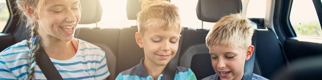 Three kids playing games in the car on a road trip